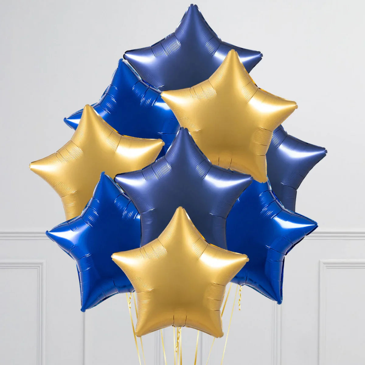 Bunch of shiny sapphire blue and gold star-shaped foil balloons against white wall