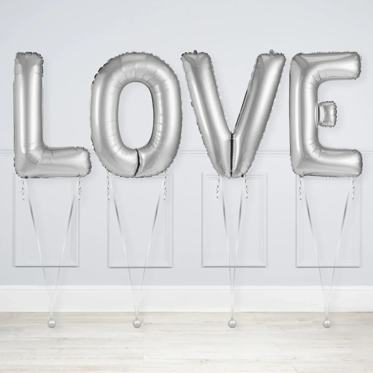 Silver foil balloons spelling LOVE inside a white room with wooden floor