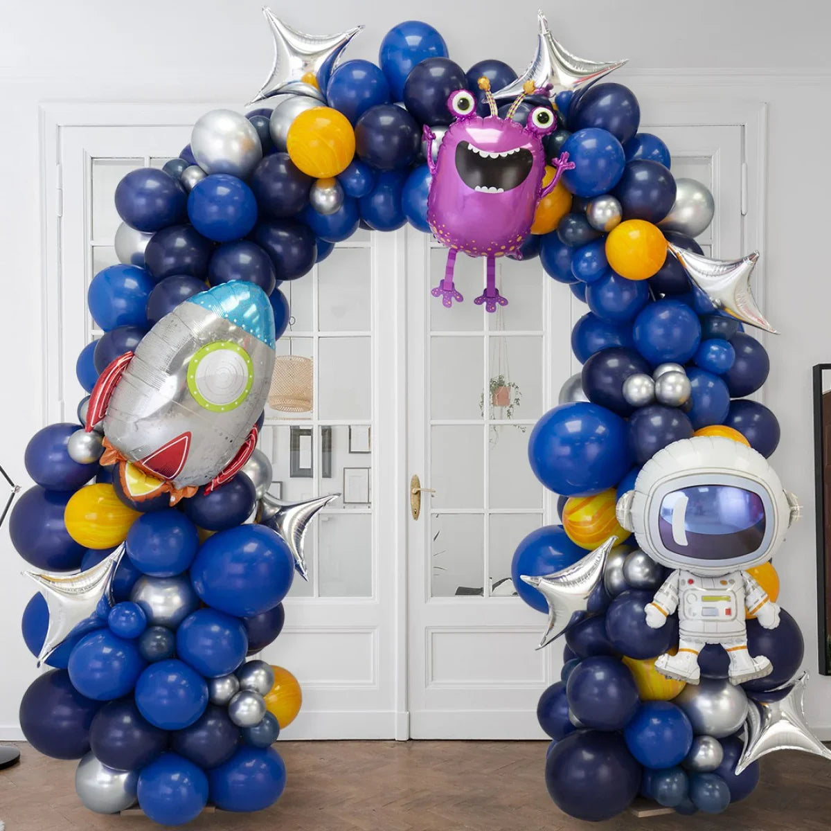 Space-themed balloon arch with blue, yellow, and silver balloons, featuring rocket, astronaut, and alien foil balloons