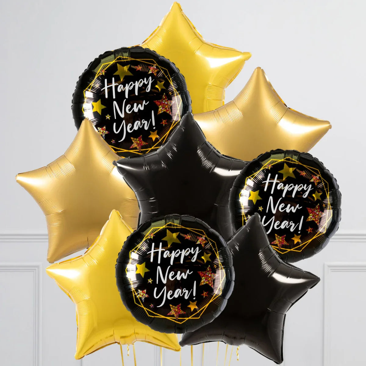 Black, gold, and yellow star-shaped and round foil balloons with Happy New Year text on white wall background
