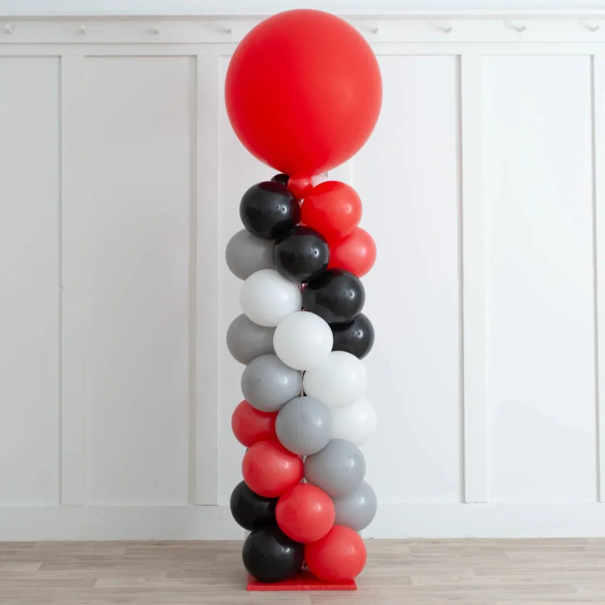 Modern spiral balloon pillar in red, black, white, and gray colors against white paneled wall