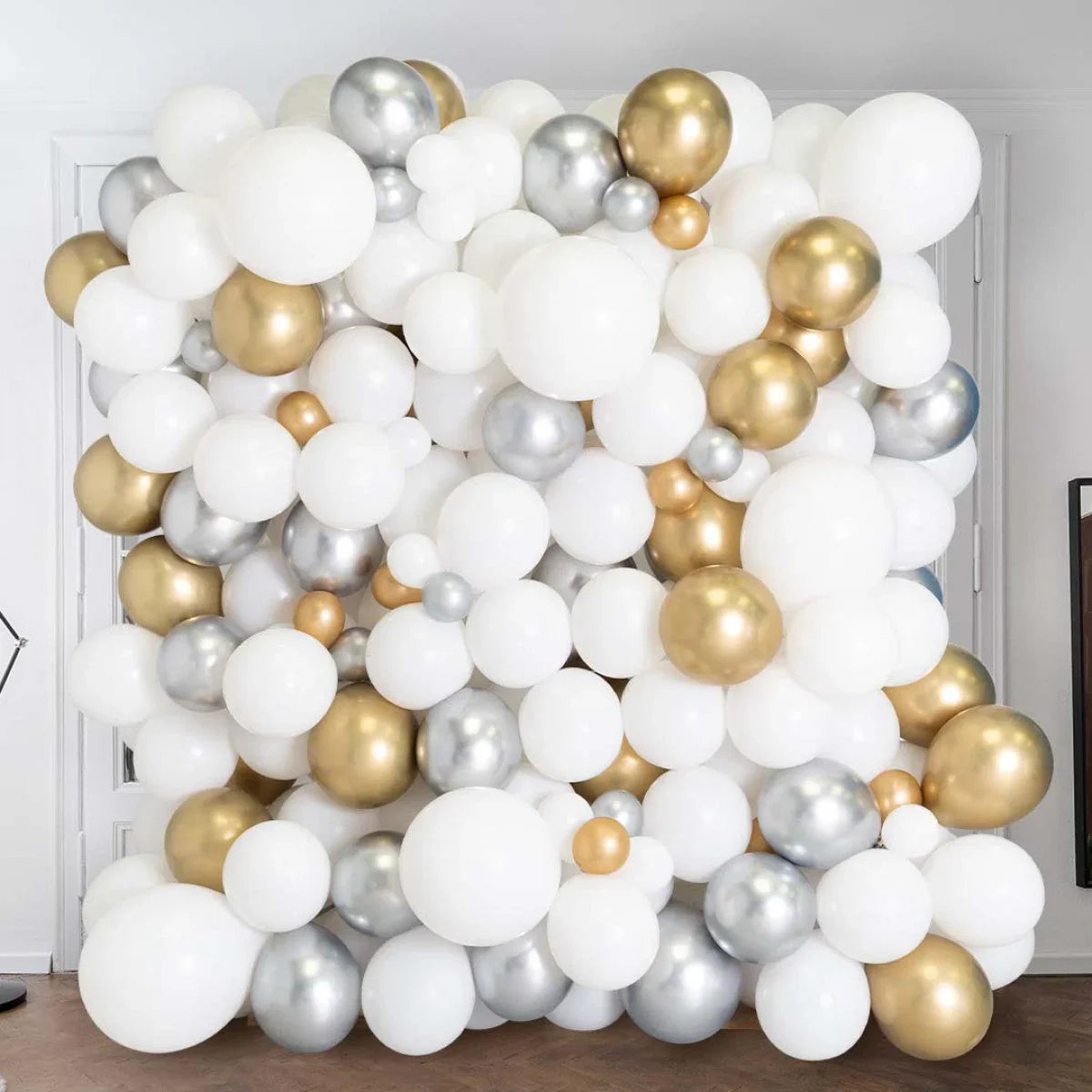Large balloon wall backdrop with white, gold, and silver metallic balloons for events