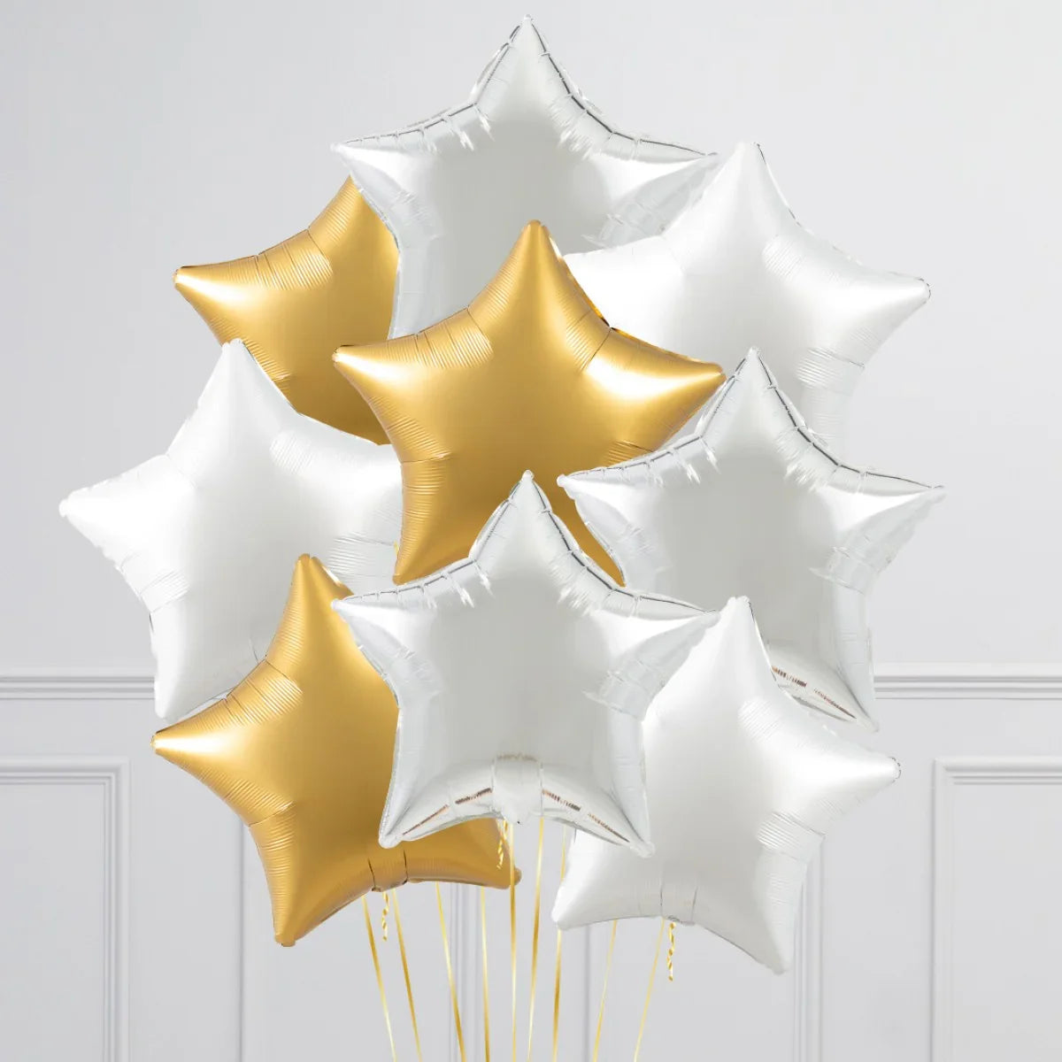 Cluster of metallic star-shaped foil balloons in gold and silver against white wall