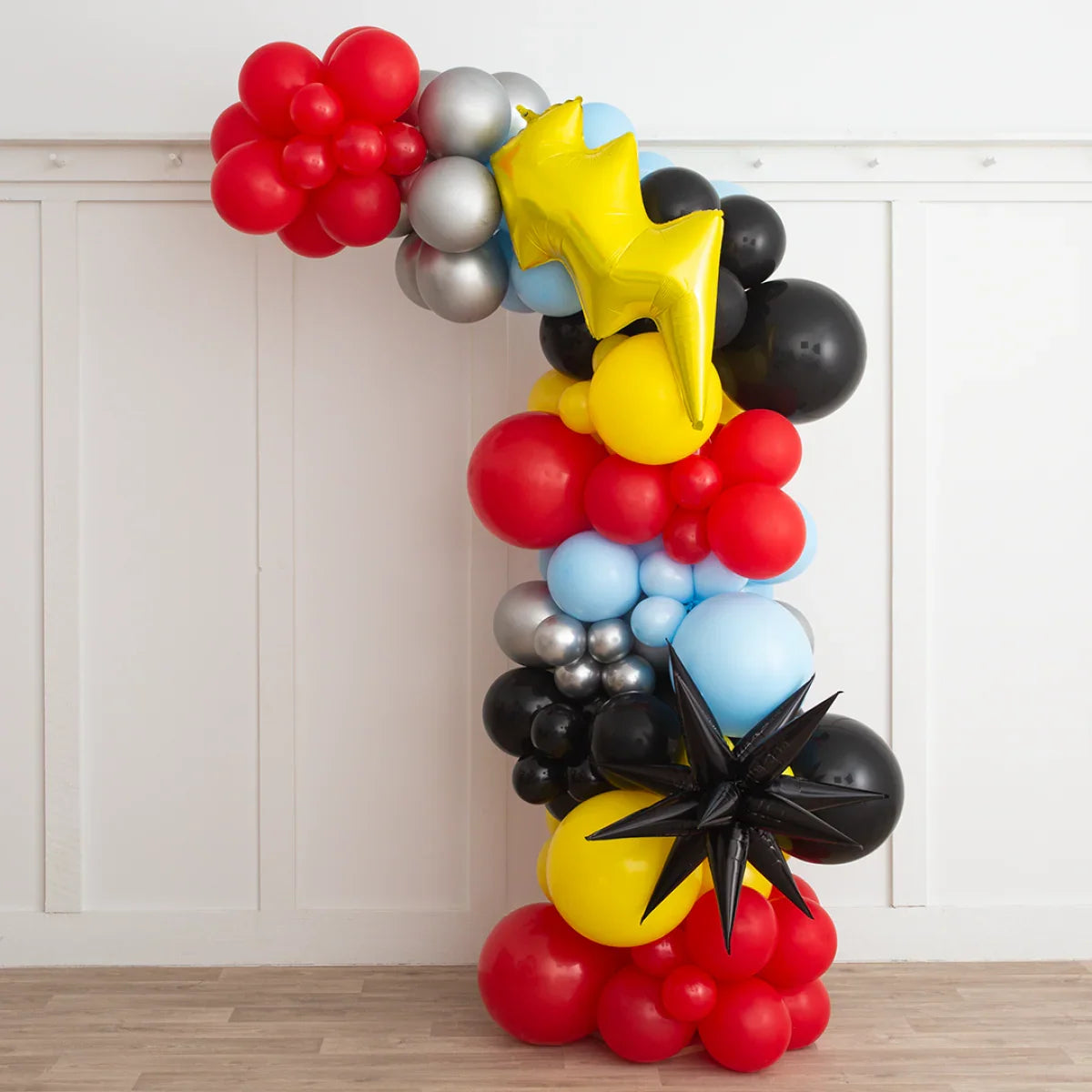 Superhero themed asymmetric balloon arch in red, yellow, black, blue, and silver colors
