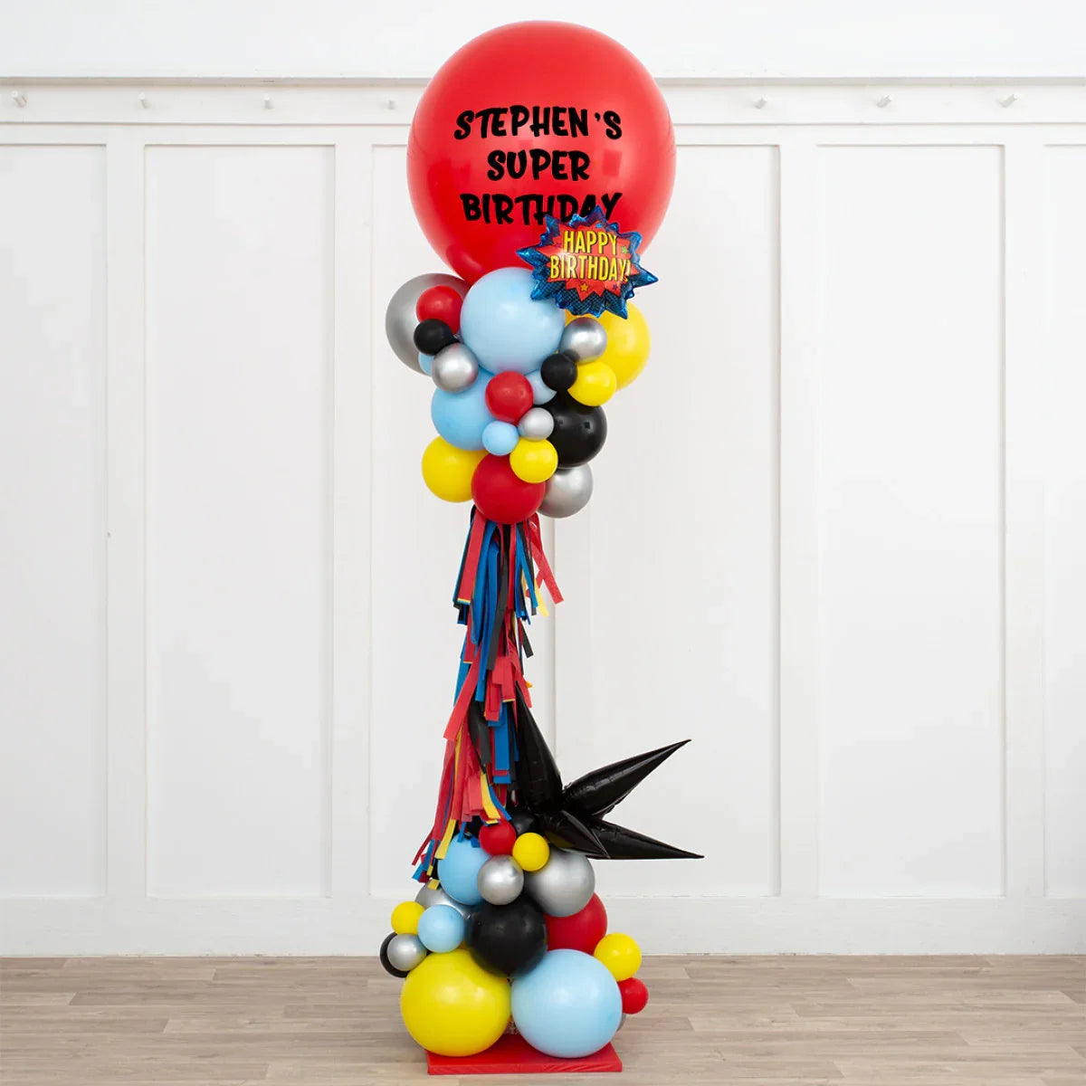 Tall colorful superhero birthday balloon pillar with red top balloon reading Stephen's Super Birthday