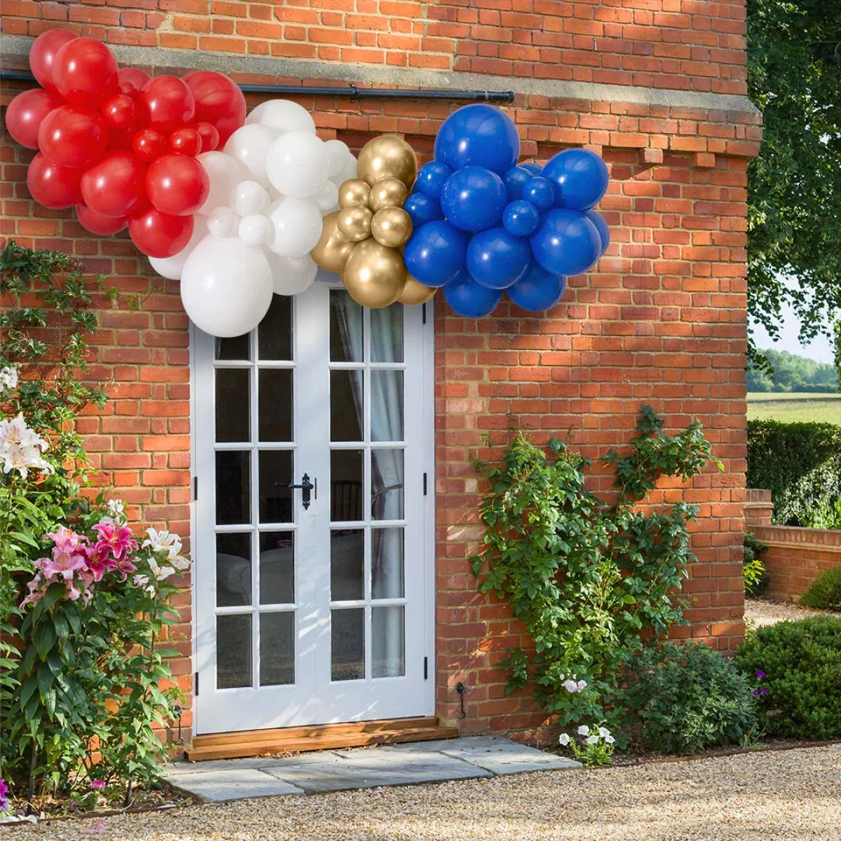 Red, white, gold, and blue balloon garland decoration above white door on brick house exterior