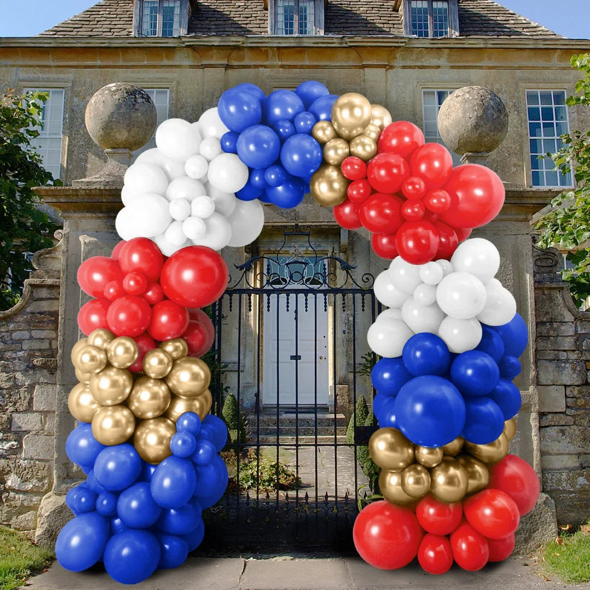 Colorful balloon arch in red, white, blue, and gold decorating stone gate entrance of classic house