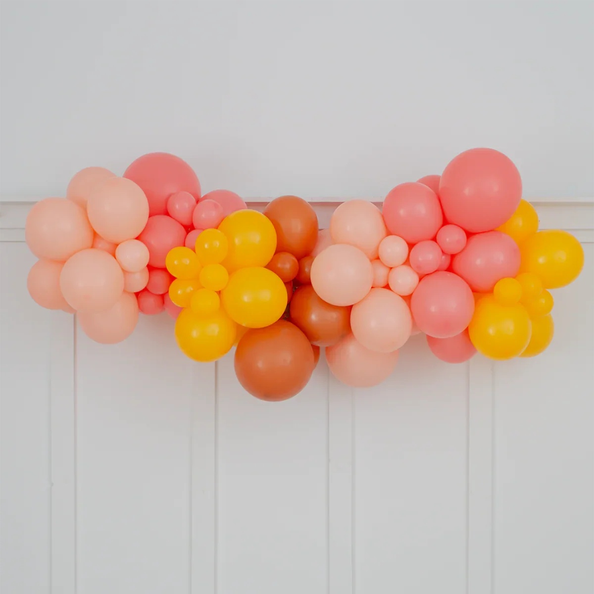 Bright tropical balloon garland in shades of pink, orange, and yellow on white wall