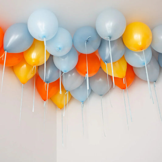 Cluster of helium-filled balloons in orange, yellow, gray, and white floating near a ceiling