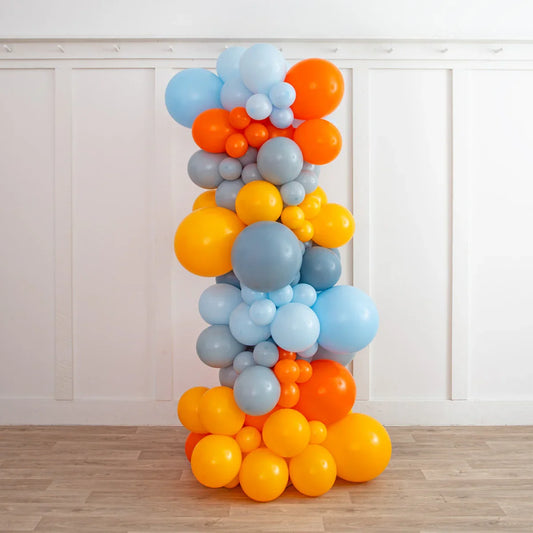 Colorful balloon pillar with orange, yellow, blue, and gray balloons against white paneled wall