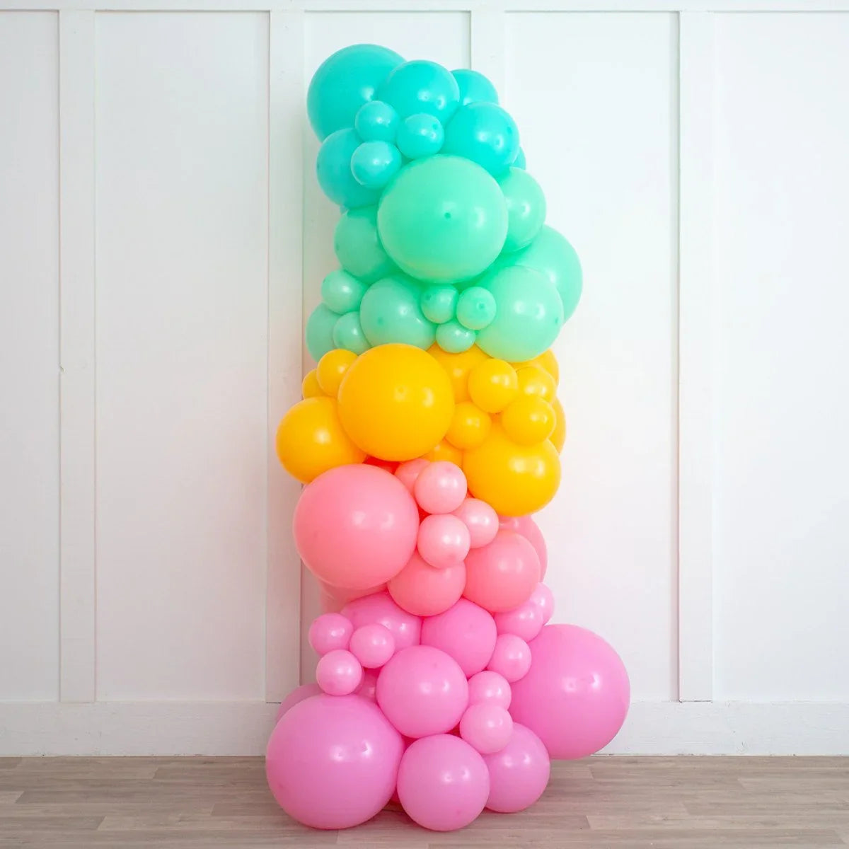Colorful inflated balloon pillar in turquoise, yellow, coral, and pink against white wall indoors