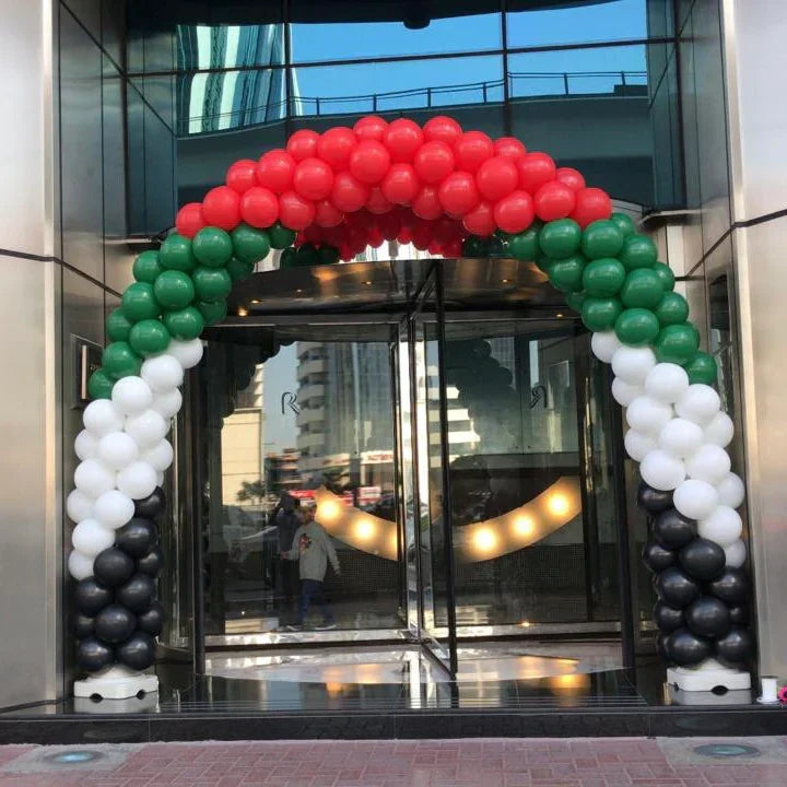 Balloon arch in red, green, white, and black colors at a glass building entrance in Dubai