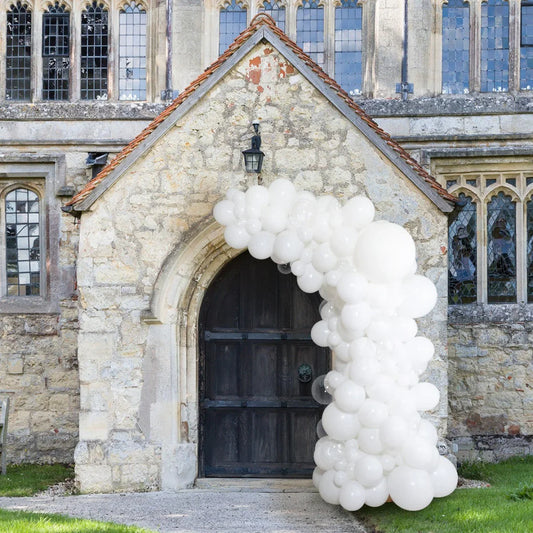White asymmetric balloon arch decorating stone church entrance with dark wooden door and stained glass windows