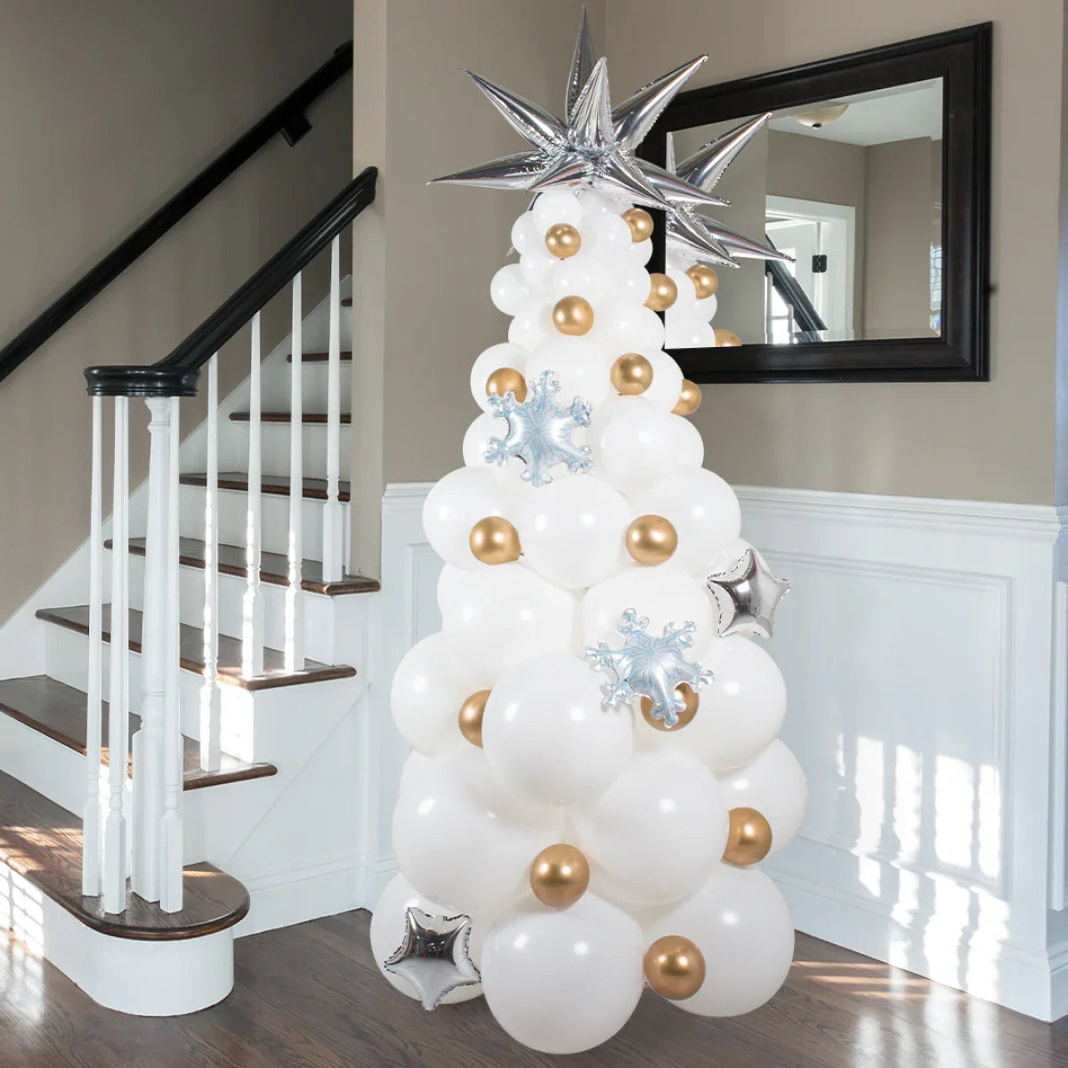 White and gold balloon Christmas tree decoration with silver star and snowflake balloons in a home foyer near a staircase
