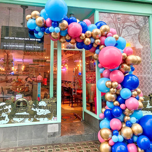 Asymmetric balloon garland in blue, pink, and gold decorating the entrance of a colorful cafe