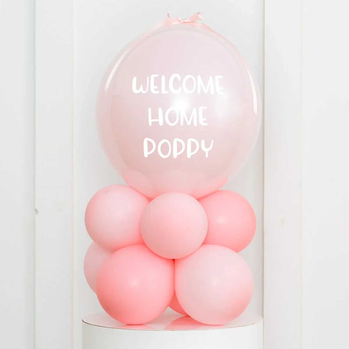 Personalised light pink helium balloon with white text welcome home poppy on pink balloon cluster