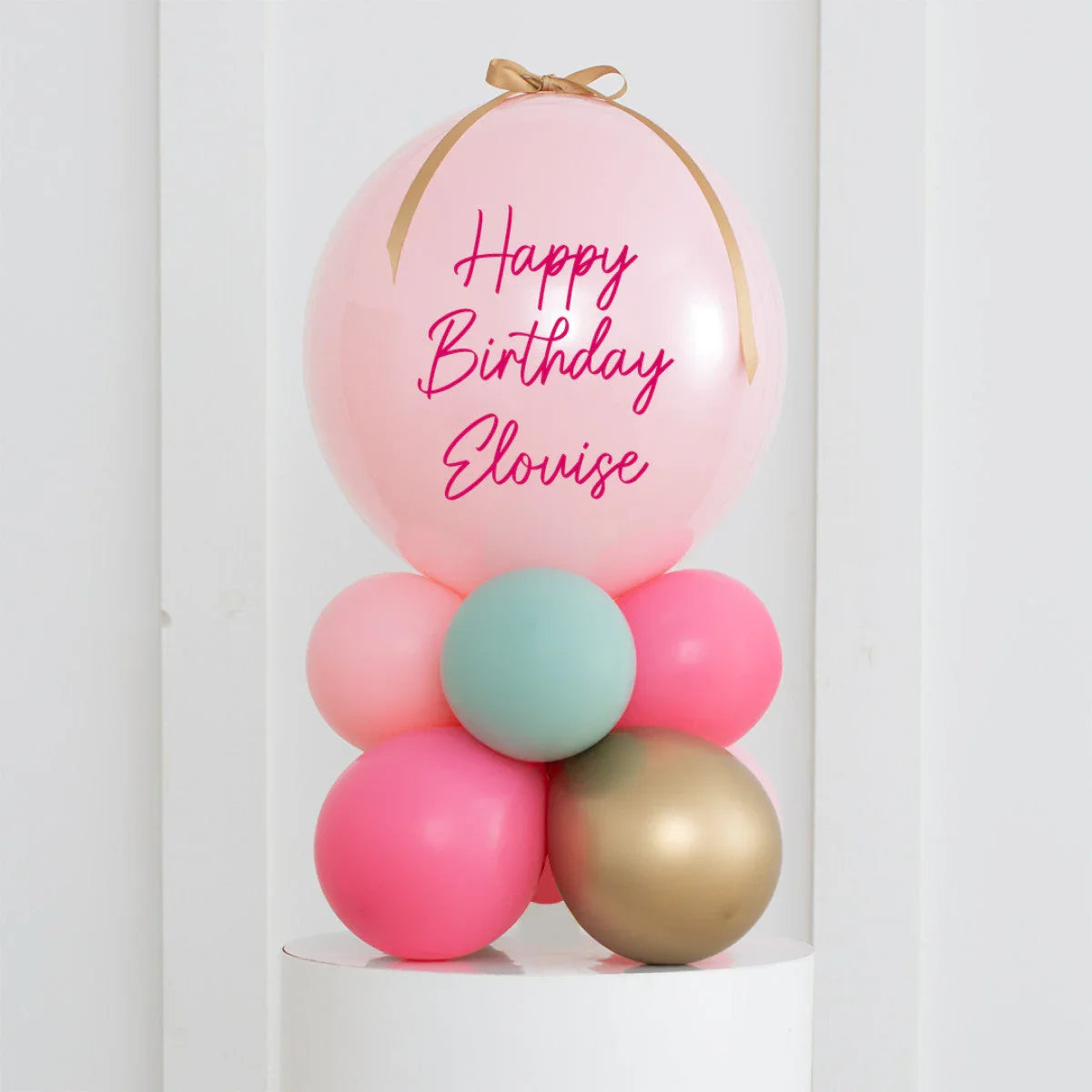 Personalized pastel pink birthday balloon with gold ribbon on multicolored balloon cluster