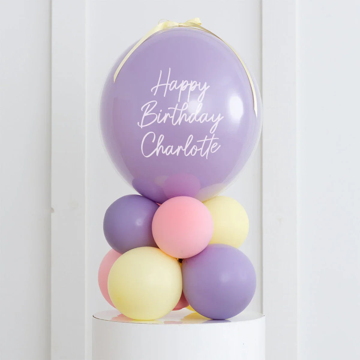 Personalized purple balloon with Happy Birthday Charlotte text and pastel balloon cluster on white pedestal