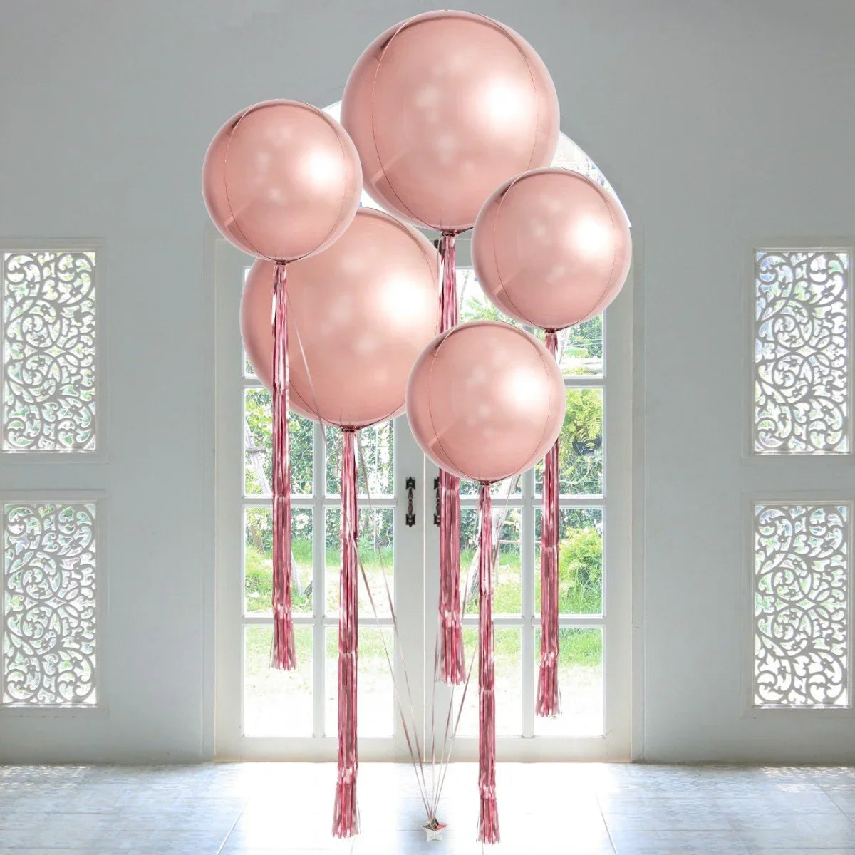 Giant rose gold orb balloons with matching tassels in bright room near white glass doors