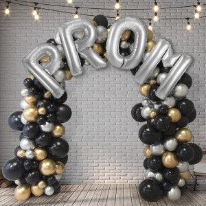 Silver prom balloon arch with black, gold, and white balloons against brick wall backdrop