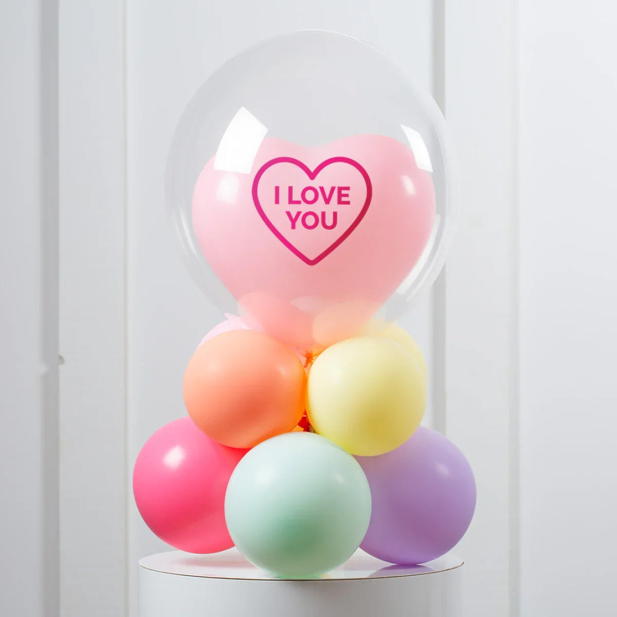 Colorful cluster of balloons with a clear balloon encasing a pink heart balloon that says I LOVE YOU