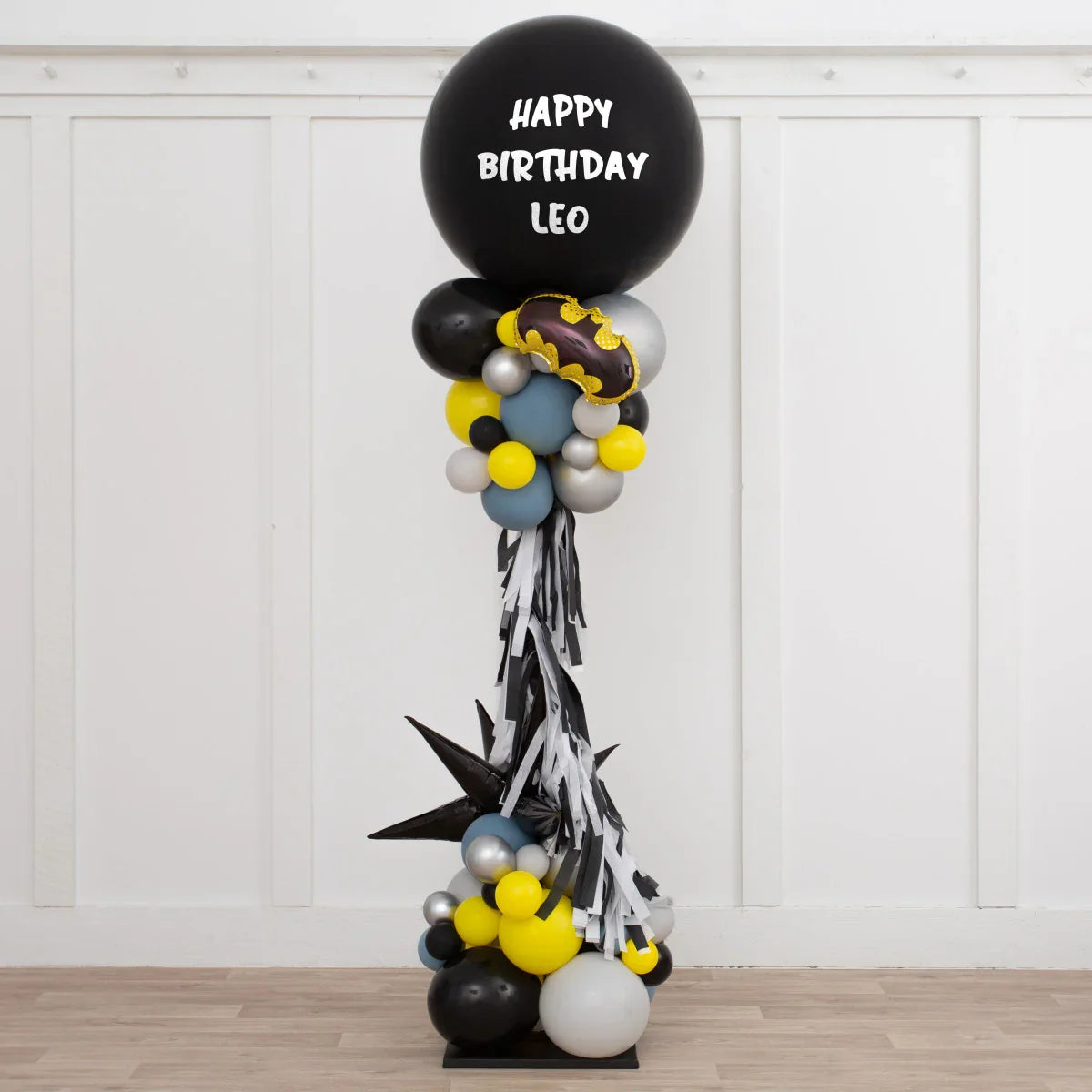 Black and yellow Batman-themed birthday balloon pillar with Happy Birthday Leo text