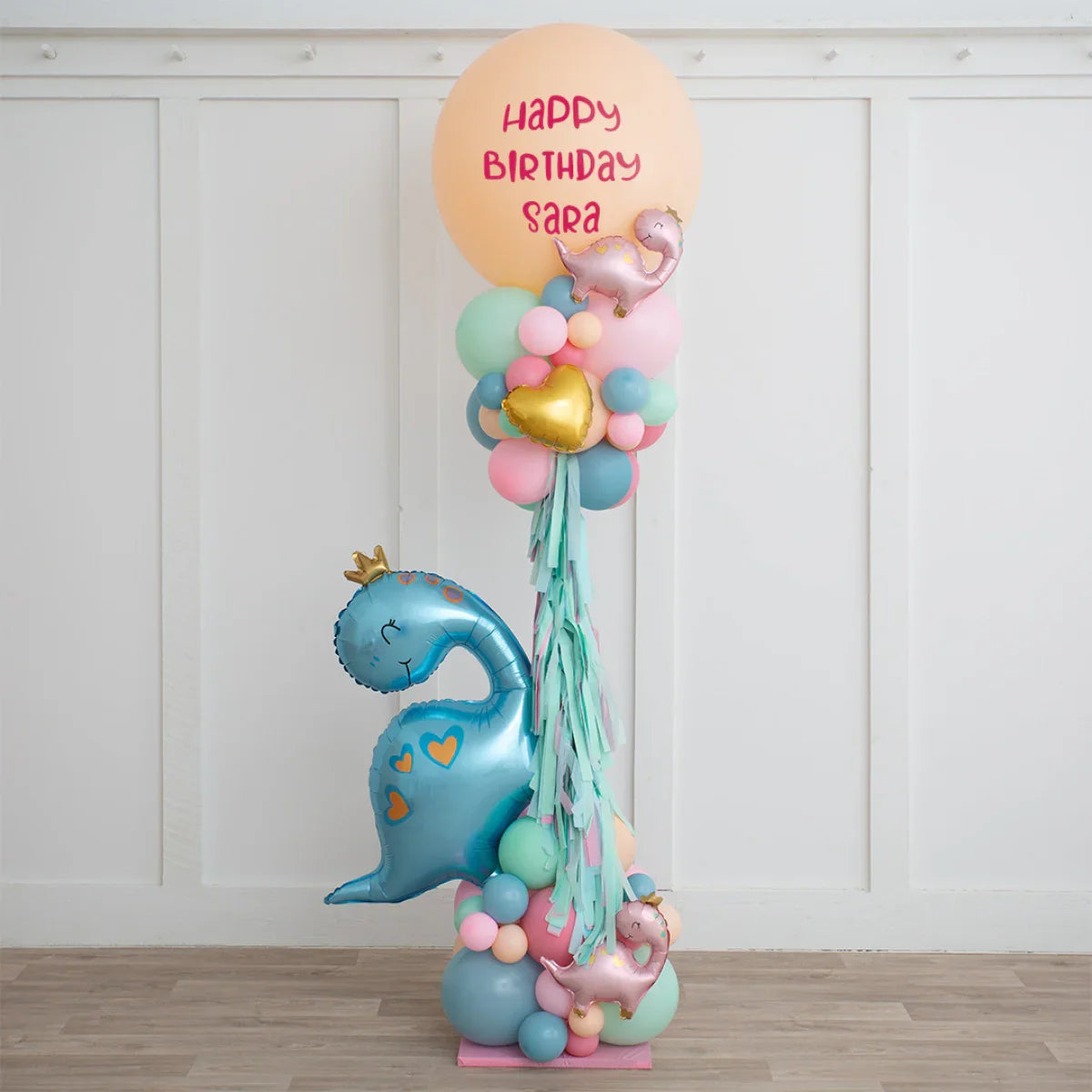 Dinosaur birthday balloon arrangement with pastel colors and 'Happy Birthday Sara' text