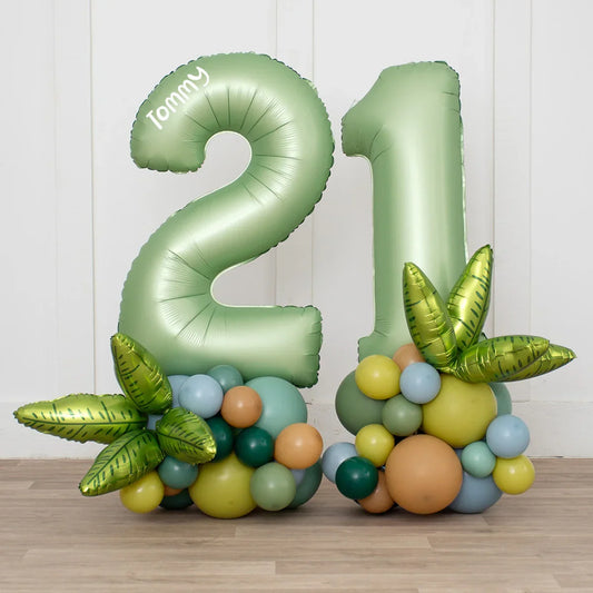 Green number 21 birthday balloons with tropical leaves and balloon clusters on wood floor