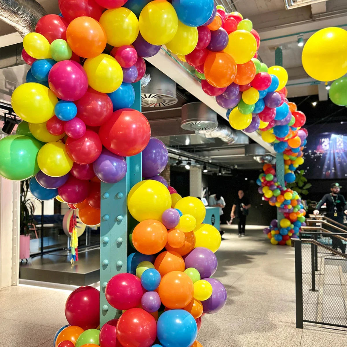 Colorful balloon garland arch with red, yellow, orange, blue, purple, and green balloons in modern indoor space