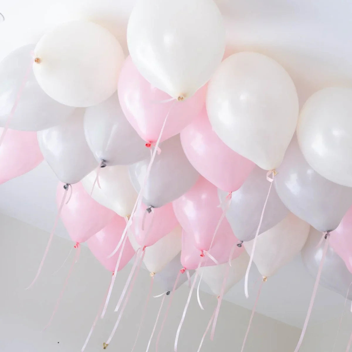 Pink and white helium balloons floating near white ceiling with ribbons