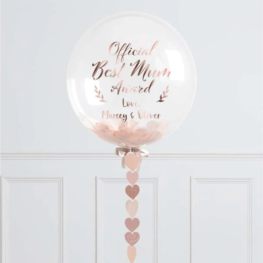 Clear balloon with 'Official Best Mum Award' text, pink confetti, and heart garland decor.