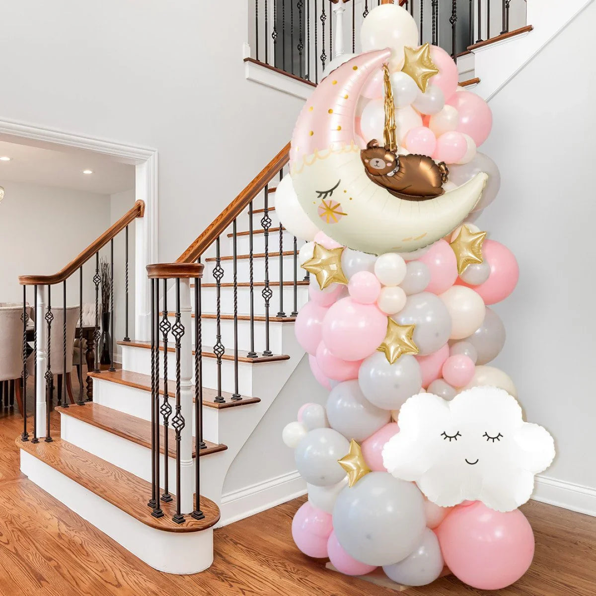 Pink and gray balloon pillar with moon, bear, stars, and cloud shaped balloons by a staircase in home