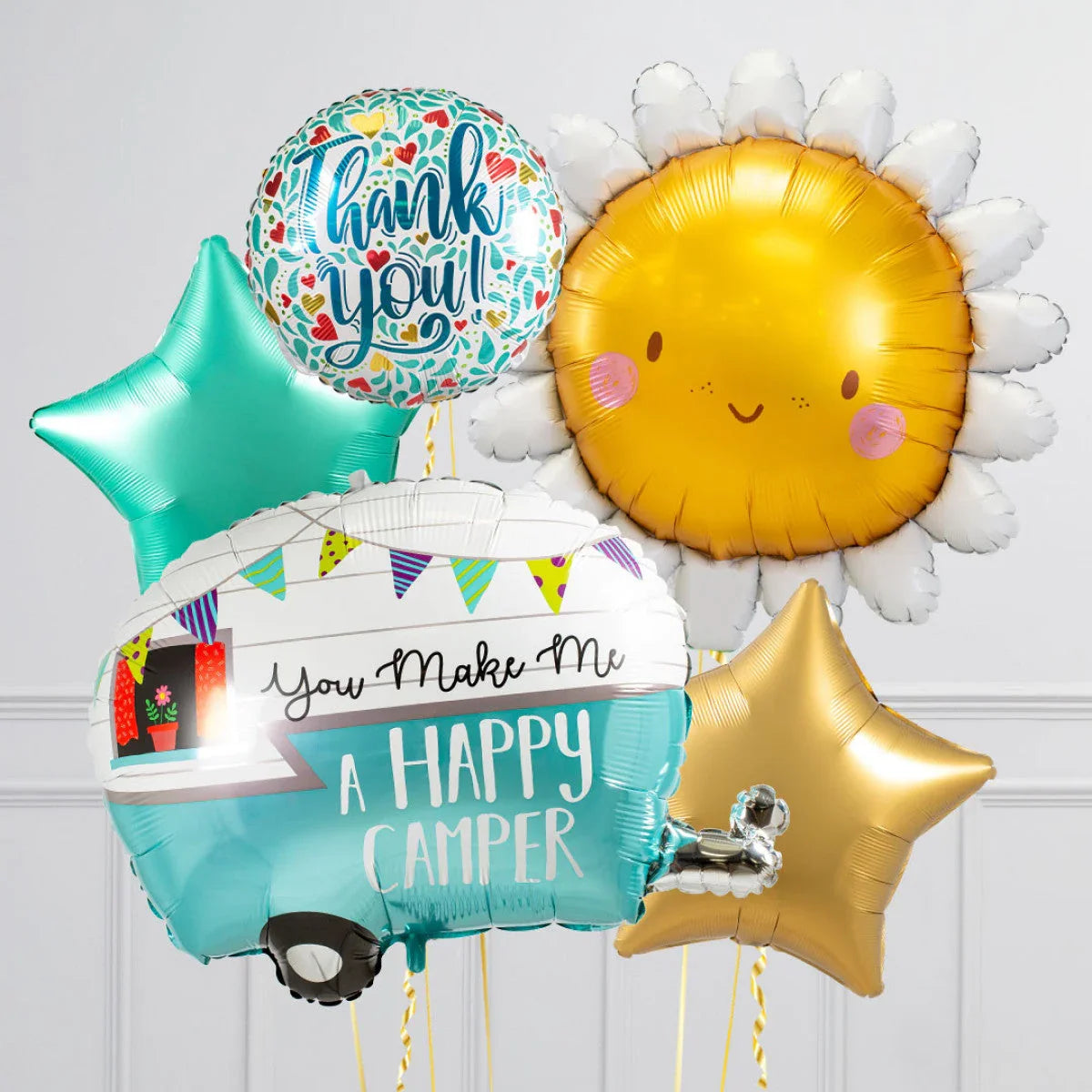 Colorful foil balloons including a cheerful sun, teal and gold stars, a 'thank you' balloon, and a camper balloon with 'You Make Me A Happy Camper' text