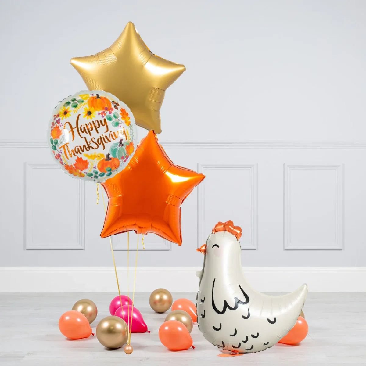 Happy Thanksgiving foil balloon with gold and orange star balloons and a chicken-shaped balloon among scattered smaller balloons
