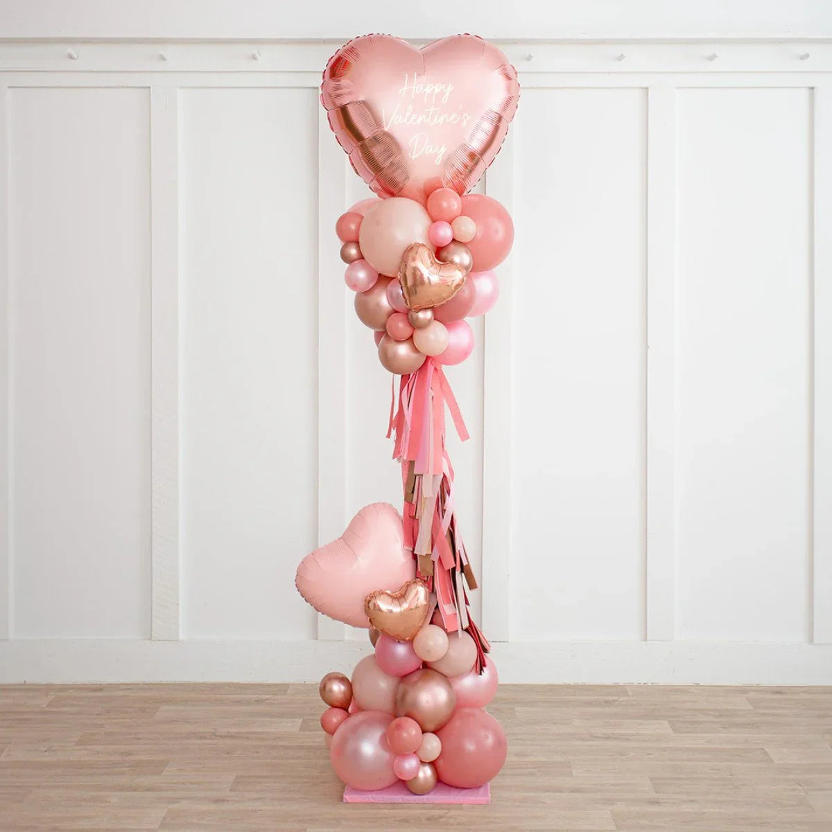 Valentine's Day balloon bouquet with pink and rose gold heart-shaped and round balloons on wooden floor