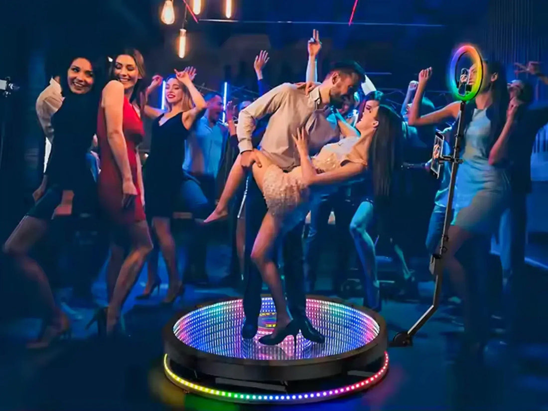 Party scene with dancing people and a couple posing on an LED-lit 360 photo booth platform