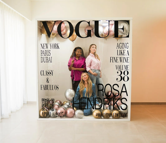 Three women posing inside a Vogue-themed photo booth with metallic balloons and birthday edition text