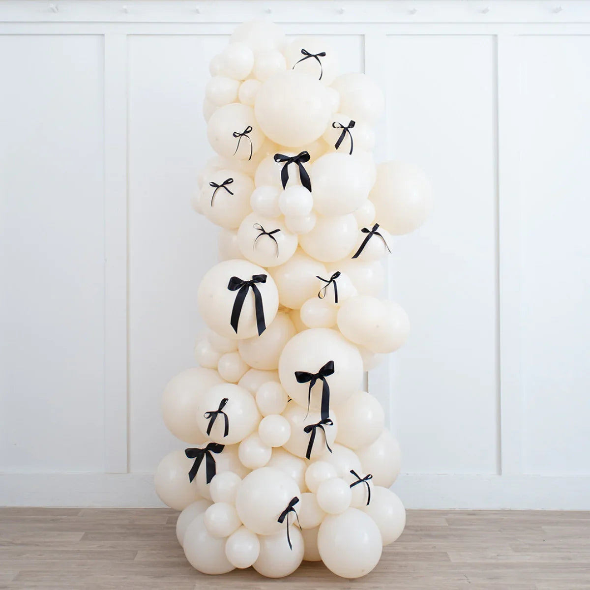 Ivory balloon pillar decorated with black bow ribbons against white paneled wall