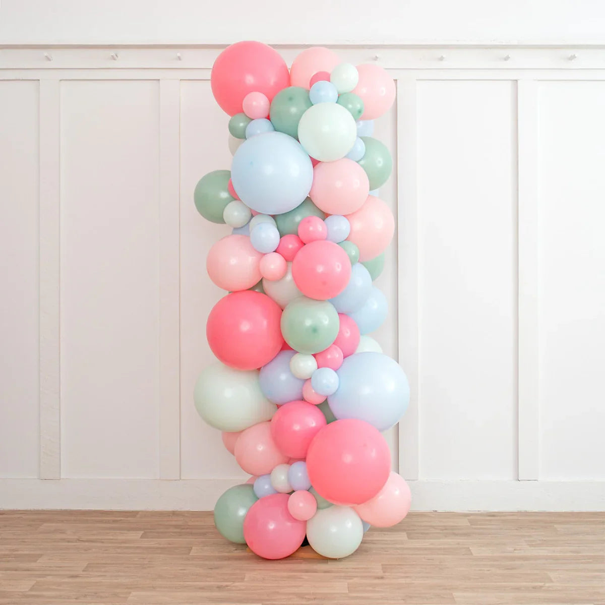 Colorful balloon pillar with pink, blue, green, and white balloons against white wall and wooden floor