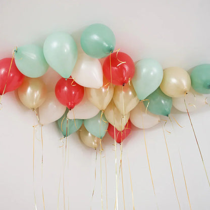 Cluster of classic Christmas helium balloons in red, green, white, and gold floating on ceiling with gold ribbons