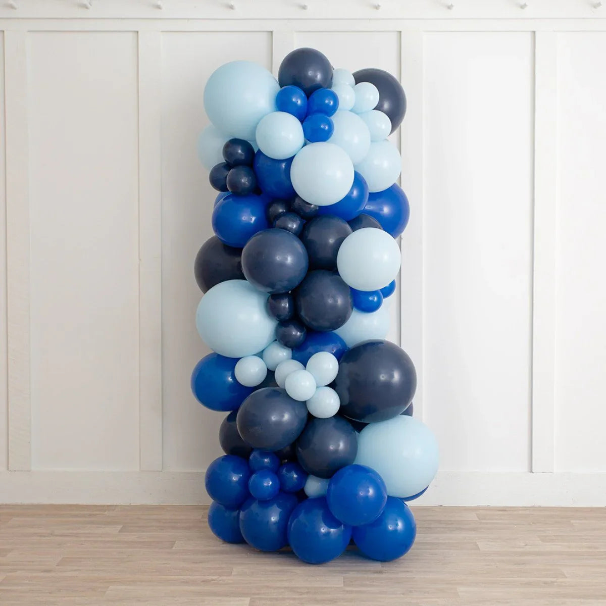 Decorative balloon pillar in shades of blue and navy against white paneled wall on wooden floor
