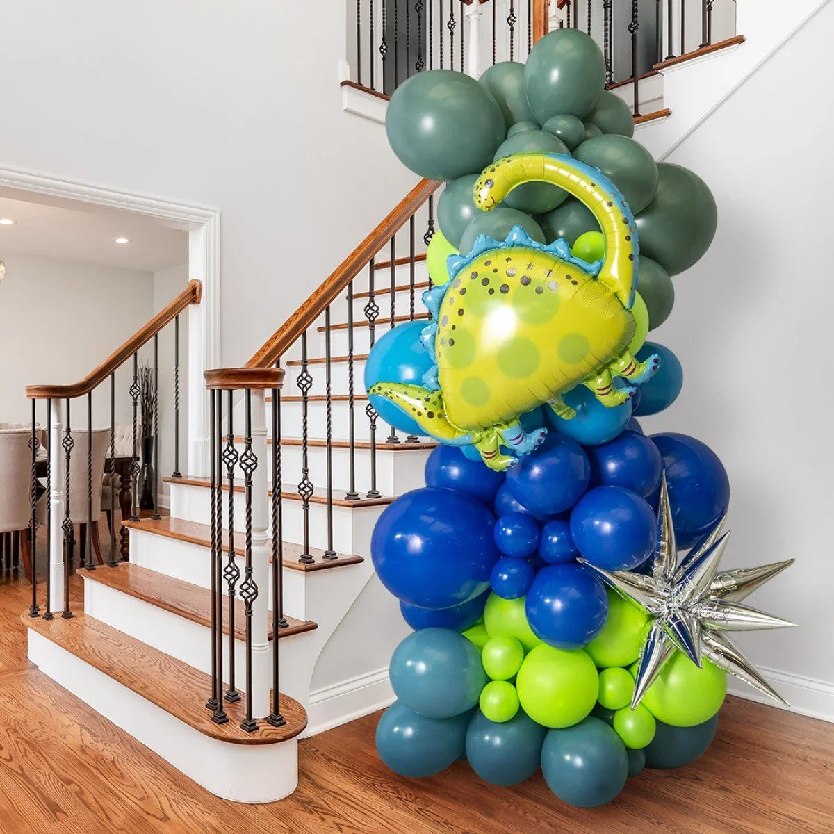 Dinosaur-themed balloon pillar with green, blue, and silver balloons near wooden staircase