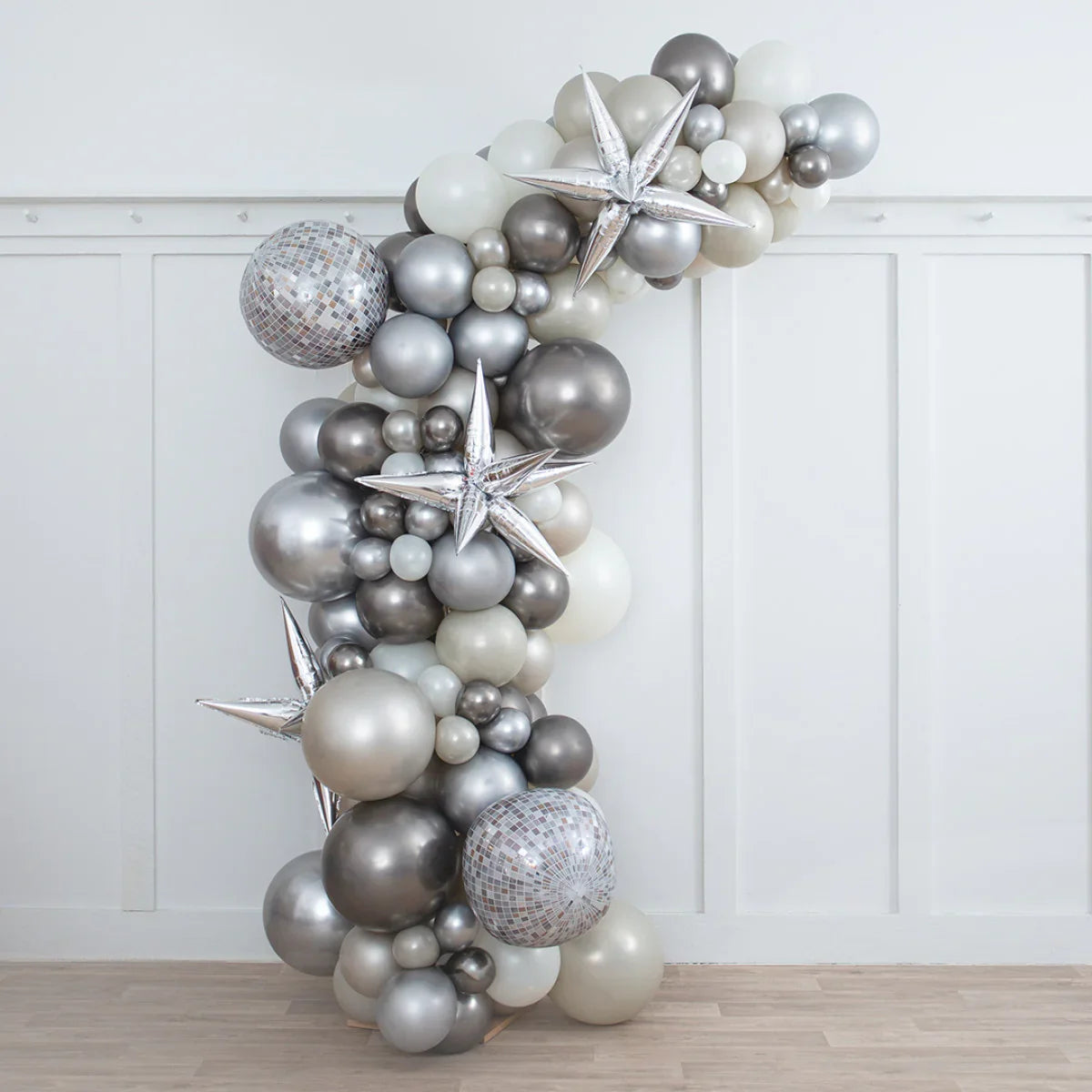 Asymmetric balloon arch with silver, white, and metallic balloons and star-shaped foils in minimal room