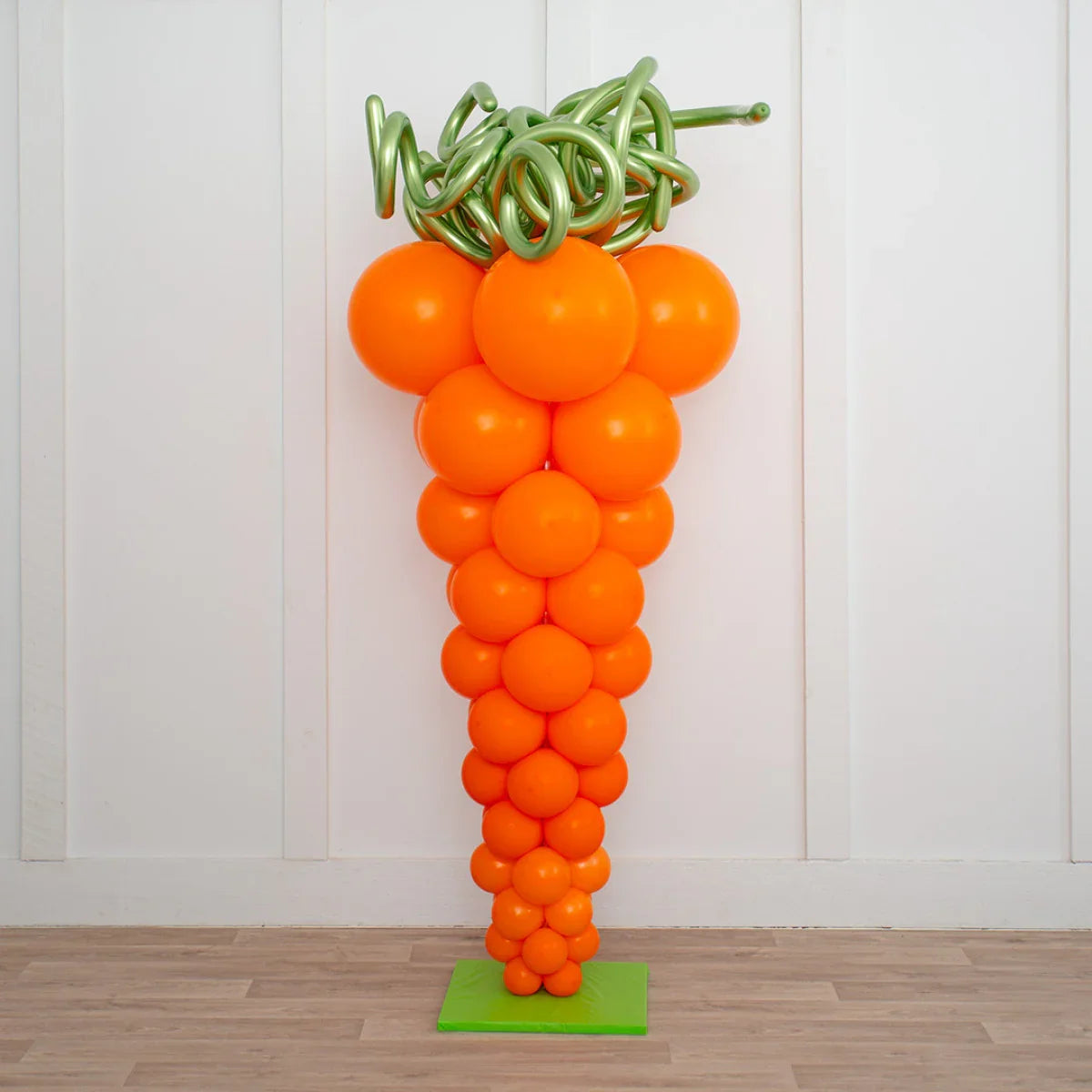 Large orange balloon pillar shaped like a carrot with green curly balloon top on green base