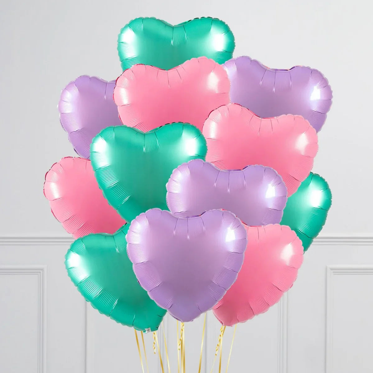 Bunch of shiny pink, green, and purple heart-shaped foil balloons with gold strings indoors