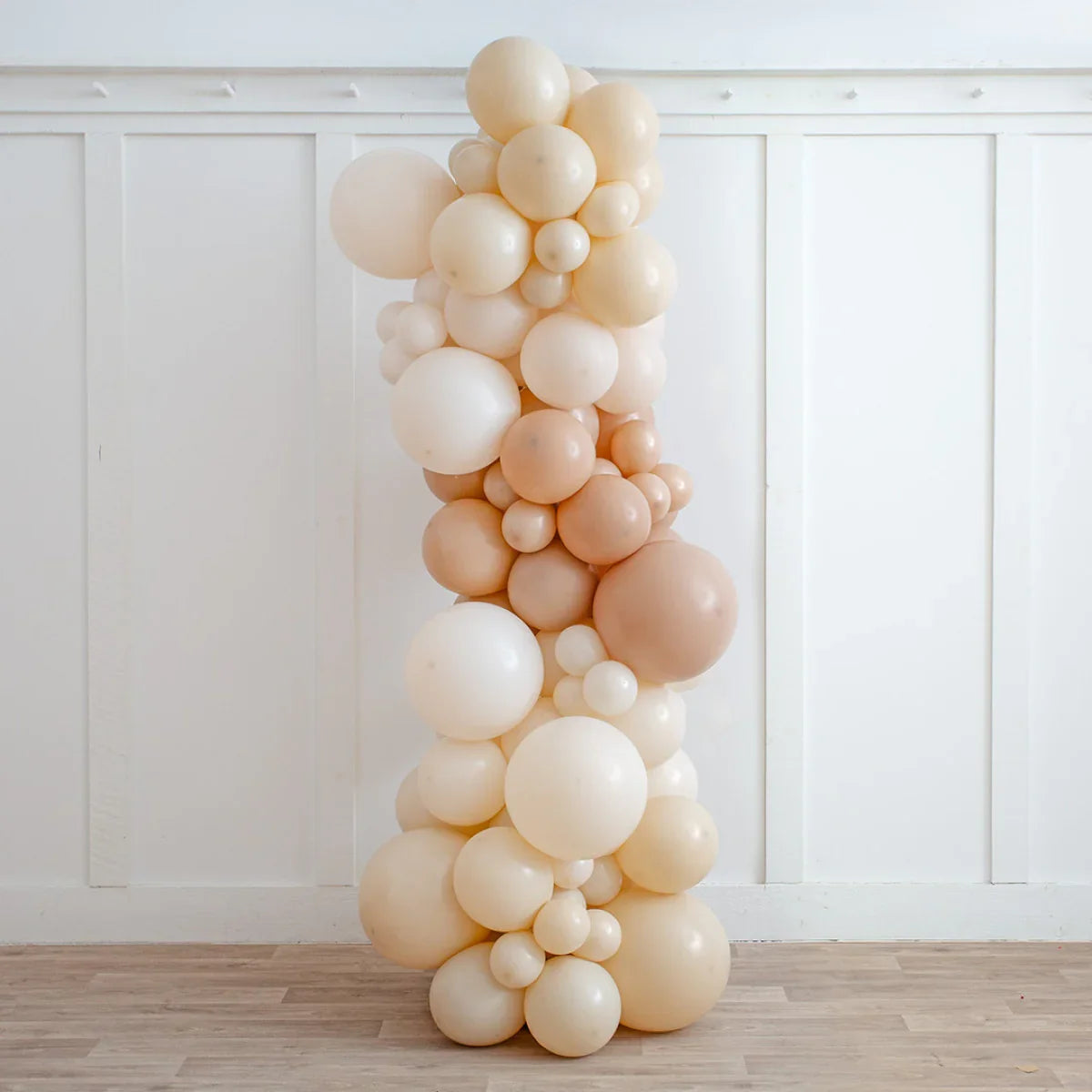 Neutral beige balloon pillar decoration in various sizes against white paneled wall on wooden floor