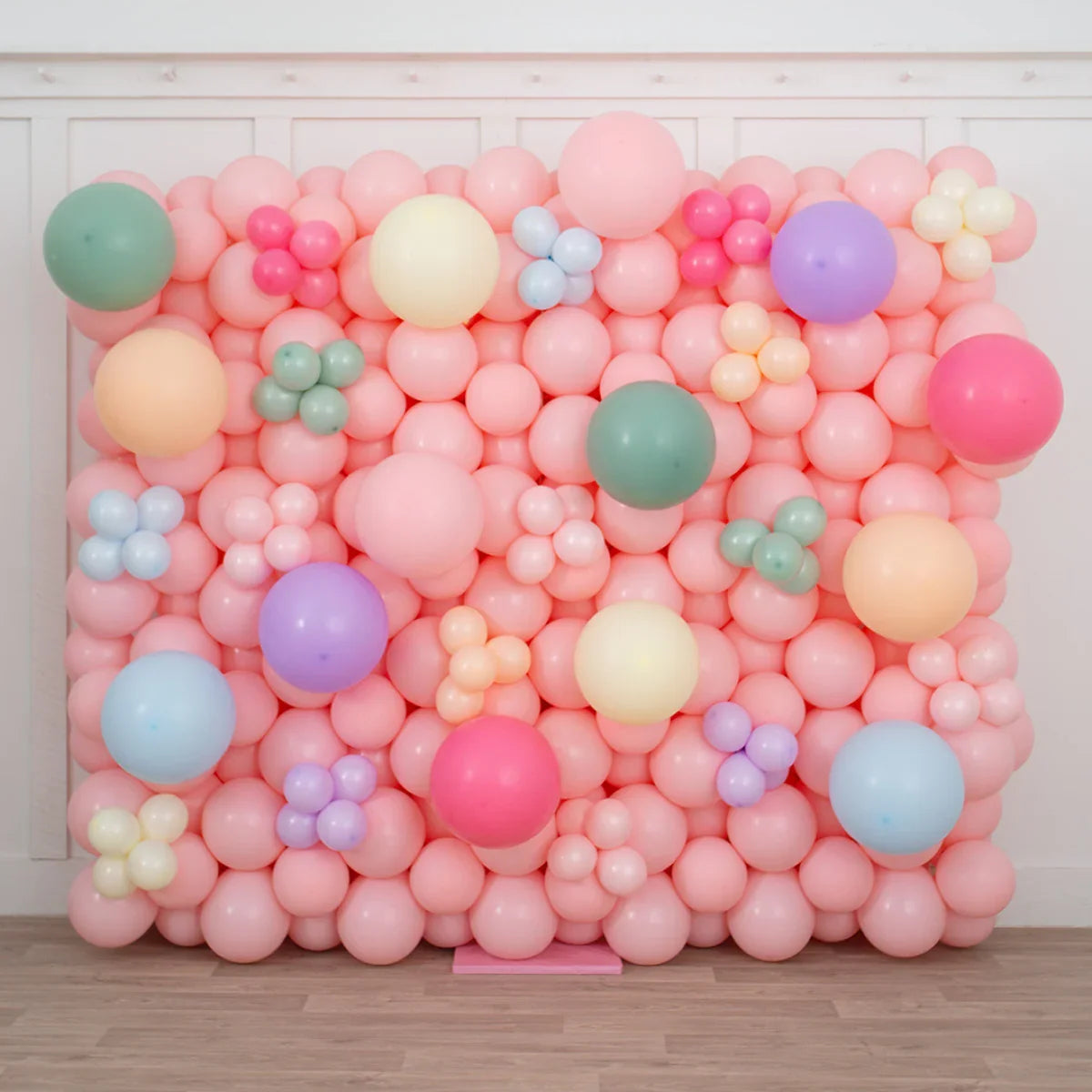 Pastel pink balloon wall with multicolored balloon clusters for party decor indoors