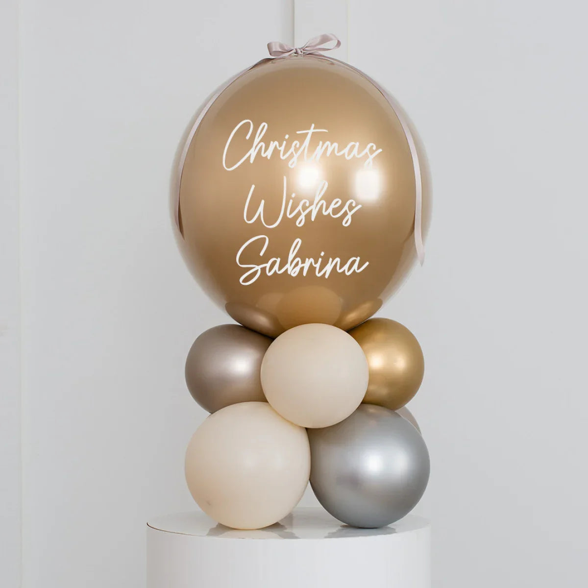 Personalised Christmas balloon decoration with 'Christmas Wishes Sabrina' text on gold bubble balloon with beige and silver balloons base