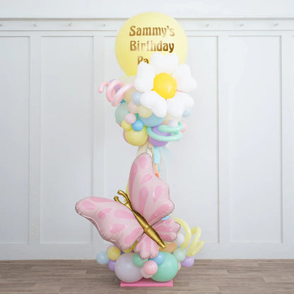 Personalised pastel balloon party pillar with pink butterfly, white daisy, and colorful balloons on wooden floor