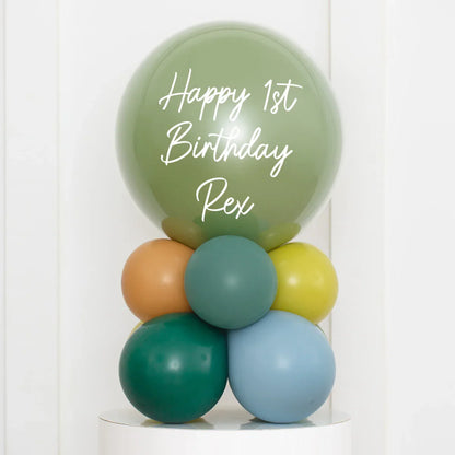 Personalized green birthday bubble balloon with text Happy 1st Birthday Rex, surrounded by smaller colorful balloons